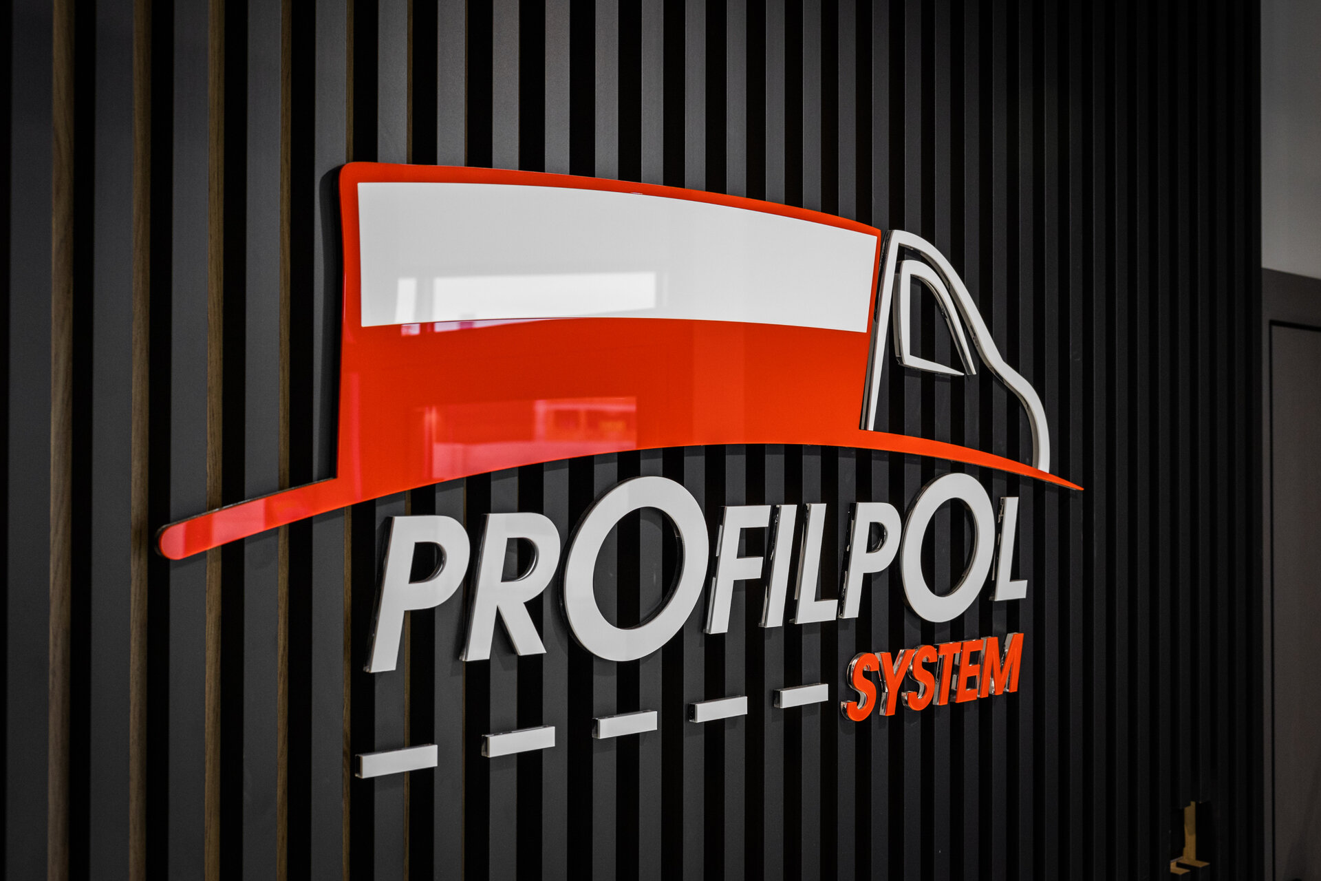 Logo firmy Profilpol na czarnej ścianie z paneli drewnianych